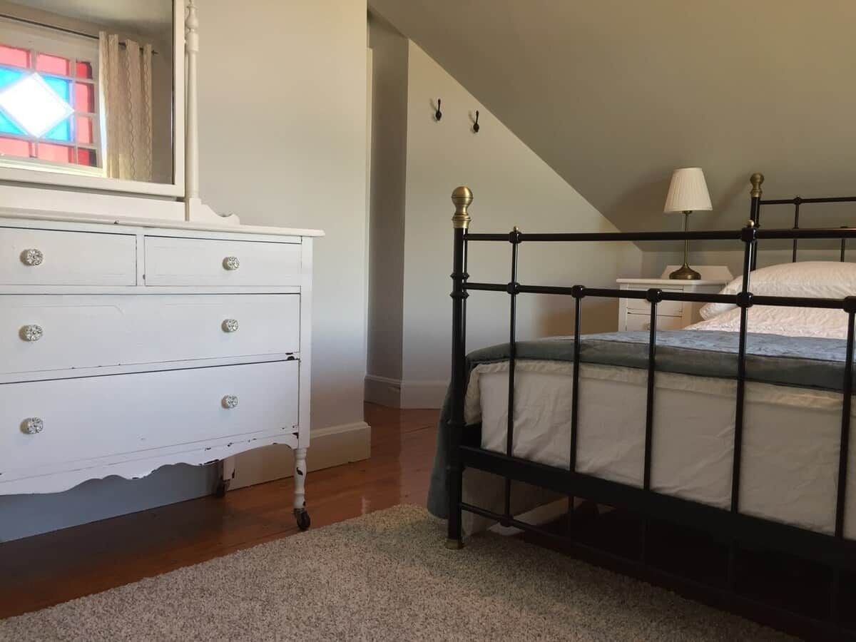 A bedroom with a bed, white dresser, and a small bedside table with a lamp.