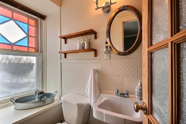 Un baño con ventana, lavamanos, inodoro, estanterías de madera y un espejo.