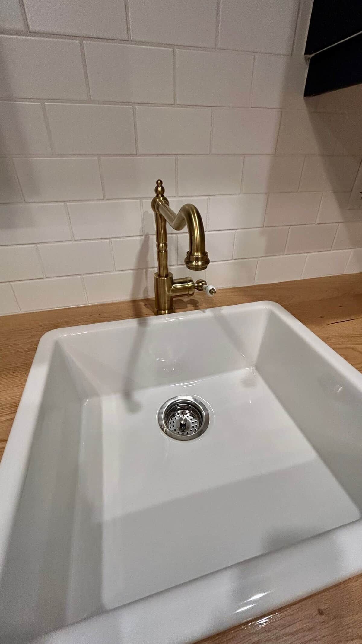 A white rectangular sink with a gold faucet, a drain, and a wooden countertop.