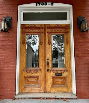 A double wooden door with a white frame, a number plaque above, and two wall-mounted lanterns on either side.