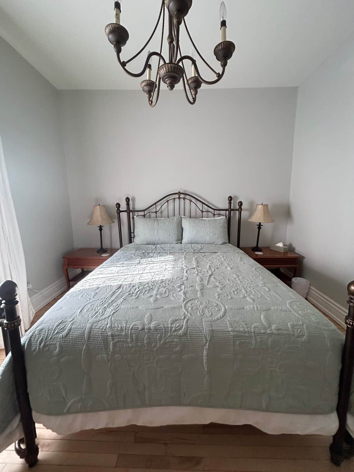 A bedroom with a bed, two bedside tables, a chandelier, and a window.