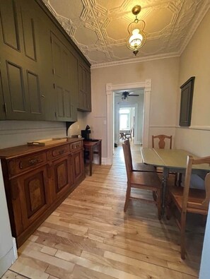 Una cocina con armarios de madera, una mesa de comedor con sillas, un ventilador de techo y un pasillo que conduce a otra habitación.