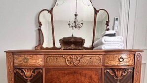 Une commode en bois ornée de sculptures complexes, un miroir et un lustre.