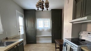 Une cuisine avec un lustre, un plancher en bois et des meubles de couleur sombre.