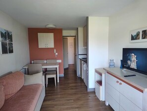 Ein gemütlicher Wohnbereich mit Sofa, Esstisch, Küchenzeile und Fernseher.