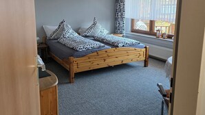 A bedroom with a wooden bed, patterned pillows, a small bedside table, and a window with curtains. - Vacation apartment in Emsland (Papenburg)