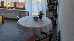 A dining area with a round table, chairs, a window with curtains, a radiator, and a patterned wall. - Vacation apartment in Emsland (Papenburg)