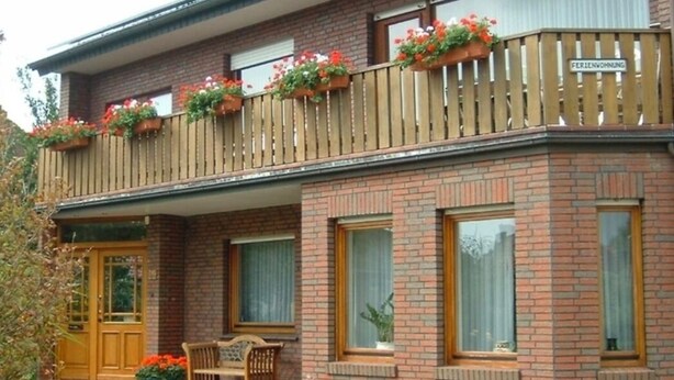 A two-story building with a balcony, a wooden fence, and flower boxes. - Vacation apartment in Emsland (Papenburg)