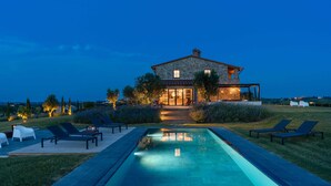 Una casa de pedra amb piscina, gandules i entrada ben il·luminada.