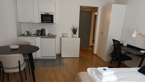 Pieni hotellihuone, jossa on sänky, työpöytä, tuoli, pieni keittiönurkkaus ja pieni kylpyhuone.