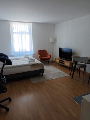 A hotel room with a bed, a chair, a desk, a television, and a window with curtains. - Charming Studio in the Perfect Spot - Stork 34 (Zürich)