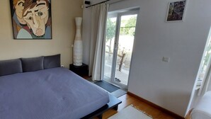 Une chambre à coucher avec un lit, une table de chevet, une lampe, un tableau et une vue à travers une porte vitrée.