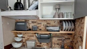 Une cuisine compacte avec des meubles blancs, un four à micro-ondes, une bouilloire et divers ustensiles de cuisine.