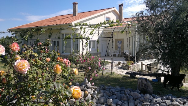Une maison avec un toit recouvert de tuiles rouges, un jardin où poussent des rosiers et un mur en pierre.