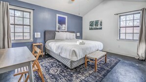 Un dormitorio con una cama, un escritorio, una silla, un ventilador de techo y dos ventanas.