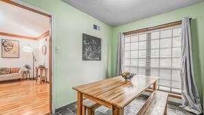 Un comedor con mesa de madera, bancos, una ventana con persianas y una pared verde.