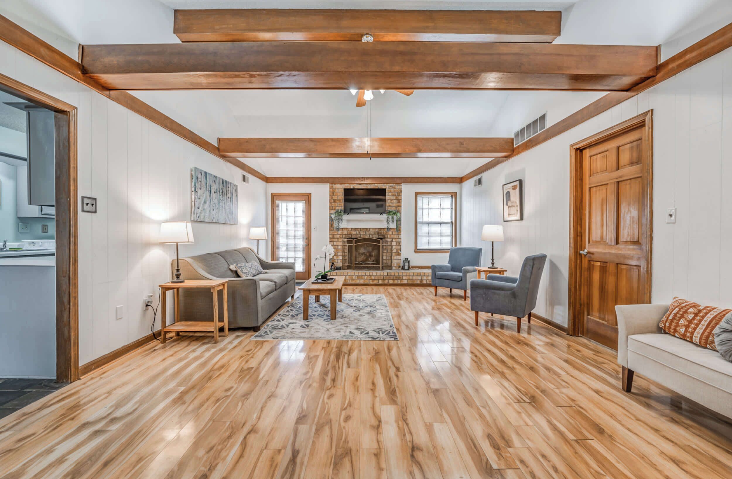 A spacious living room with hardwood flooring, a fireplace, and a kitchen visible through an open door.