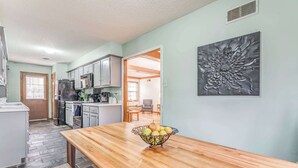 Una cocina con una mesa de madera, un frutero y un adorno metálico en la pared.