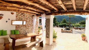 A rustic interior with a stone wall, wooden ceiling, and a view of a pool and mountains.