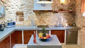 A kitchen with a stone wall, a microwave, a sink, a wooden cabinet, and a fruit bowl on the counter. - Villa 'Sa Paissa De Can Sergent' with Mountain Views, Wi-Fi, and Air Conditioning (Cala Vedella)