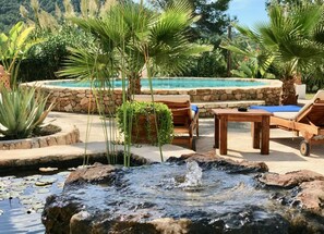 A pool area with a waterfall feature, lounge chairs, and a stone wall.