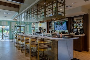 Eine Bar mit einer Marmor-Arbeitsplatte, mehreren Hockstühlen und einem Fernseher, der ein Sportspiel zeigt.