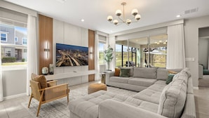 A modern living room with a large flat-screen TV, a sectional sofa, a wooden chair, and a dining area with a view. - Last Minute Disney Getaway! Luxury Villa with Private Pool, Game Room & Themed Bedrooms. Book Now! #150127 (Orlando)
