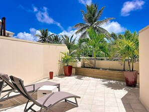 Eine Dachterrasse mit Lounge-Möbeln, Blumentöpfen und blauem Himmel.
