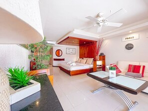 Ein modernes Hotelzimmer mit Bett, Sofa, Esstisch und Deckenventilator.