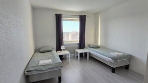 A small, single-room apartment with two single beds, a small table, a chair, and a window with curtains. - Cozy apartment near Volvo Cars (Gothenburg)