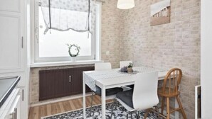 A dining area with a white table, chairs, a hanging light fixture, a window with curtains, and a brick wall. - Cozy apartment near Volvo Cars (Gothenburg)
