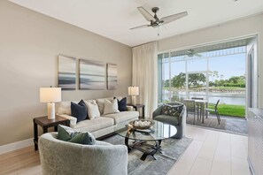 Ein modernes Wohnzimmer mit einer Couch, einem Sessel, einem Glastisch und Blick auf einen See durch große Fenster.