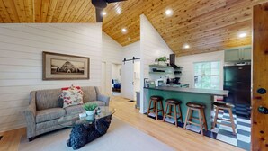 Een modern interieur met een houten plafond, een zithoek met een bank en salontafel, een keuken met barstoelen, en een koelkast.