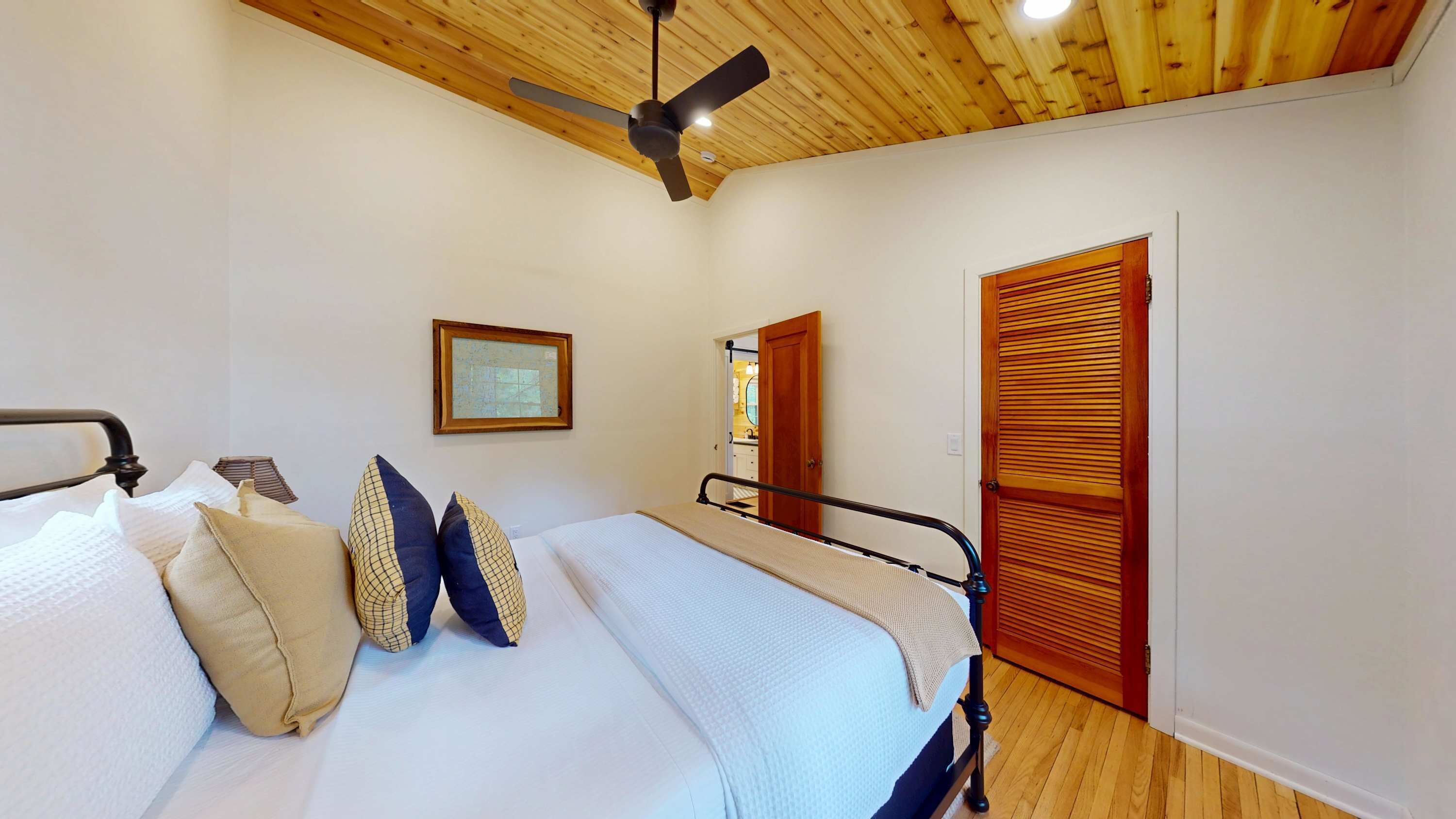 Une chambre à coucher avec un lit, des oreillers, un ventilateur de plafond, un tableau encadré et des portes en bois.