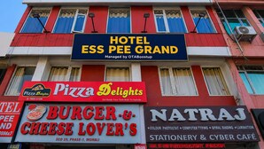 Un immeuble à plusieurs étages, sur lequel on peut voir des enseignes indiquant : Hôtel Ess Pee Grand, Pizza Delights, Burger & Cheese Lover's et Natraj Stationery & Cyber Café.