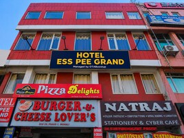 Un edificio de varios pisos con letreros que indican Hotel Ess Pee Grand, Pizza Delights, Burger & Cheese Lover's y Natraj Stationery & Cyber Café.