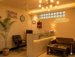 Un área de recepción con mostrador, un reloj, un letrero en la pared, una planta en maceta, un sofá y una mesita de centro.