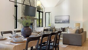 A dining area with a wooden table, chairs, and a large vase of flowers. There is a sofa and a painting on the wall. - 6 BR Mountain Golf Retreat, Hot Tub, Fall Foliage Views, Trailhead Steps Away (Avon)