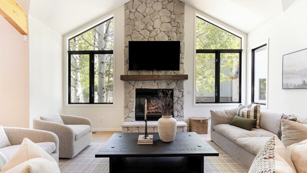 A spacious living room with a stone fireplace, large windows, and a flat-screen TV. - 6 BR Mountain Golf Retreat, Hot Tub, Fall Foliage Views, Trailhead Steps Away (Avon)