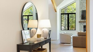 A modern living room with a fireplace, a large window, and a console table with decorative items. - 6 BR Mountain Golf Retreat, Hot Tub, Fall Foliage Views, Trailhead Steps Away (Avon)