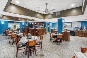 A spacious dining area with multiple tables and chairs, a kitchen area, and a ceiling fan. - Oceanfront Condo with Lazy River (North Myrtle Beach)