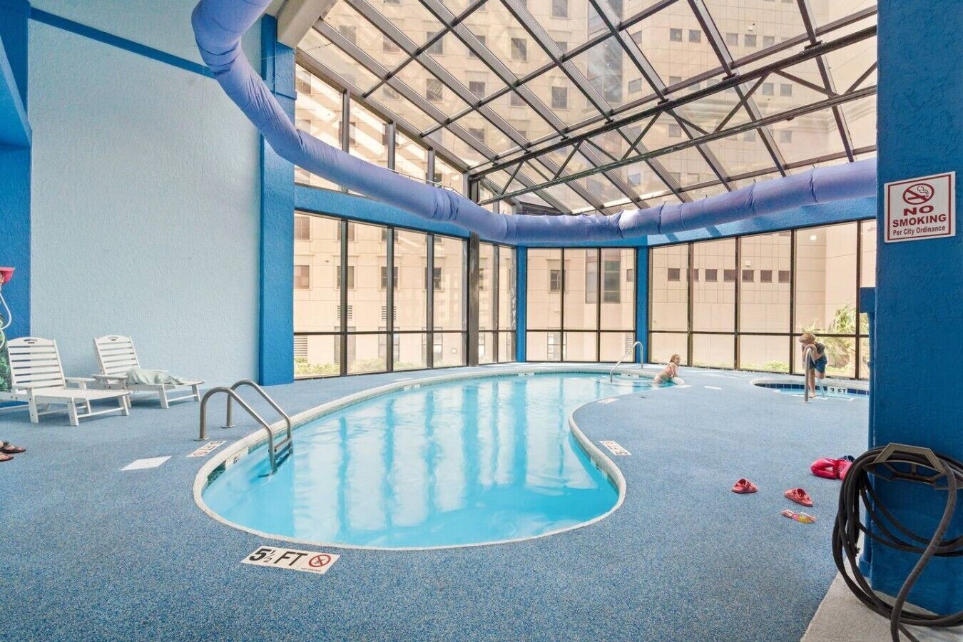 En indendørs swimmingpool med klare glaslofter, blå vægge og et skilt med røgfrit område.