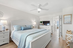 Ein Schlafzimmer mit Bett, Nachttischen, Fernseher und Deckenventilator.