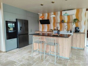 Una cocina moderna con una isla central, taburetes de bar, horno empotrado y televisor de pantalla plana.