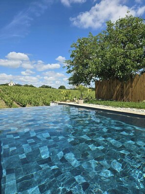 A clear swimming pool with a wooden deck and a large tree in the background. - Wine barn with pool in the heart of Layon (Val-du-Layon)