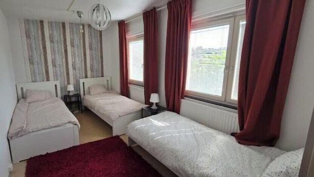Un dormitorio con dos camas individuales, alfombra roja y una ventana con cortinas.