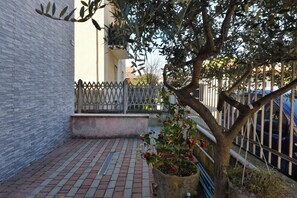Une cour avec un sol en briques, un arbre, une clôture blanche et un bâtiment doté d’un balcon.