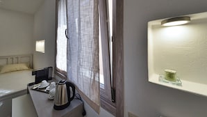 Une chambre d’hôtel avec un lit, une table de chevet avec une bouilloire, des tasses et une petite étagère avec une bougie.