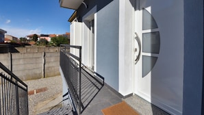 L’extérieur d’un bâtiment avec une porte blanche, une rambarde en métal noir et un mur en béton.