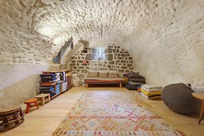 An interior with a stone wall, a bed, a bench, a rug, and a small stool.